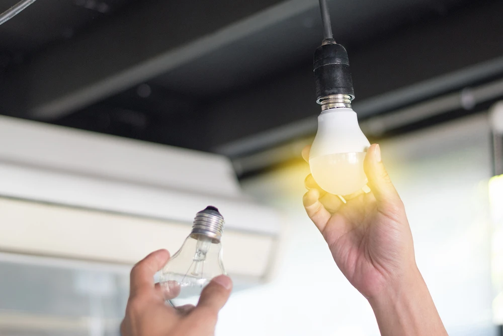 Hands changing out an incandescent bulb for an LED bulb.