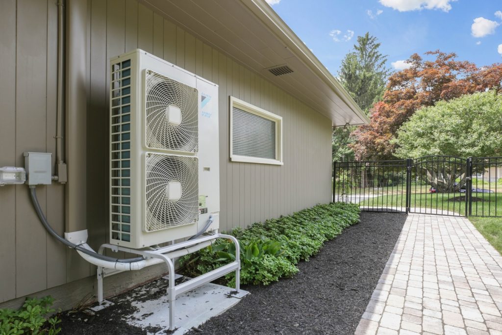brand-new heat pump condenser outdoor unit against the side of home exterior in flowerbed