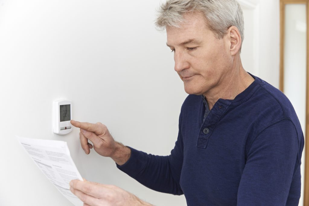 mature man reviewing the thermostat to make a cold house warmer