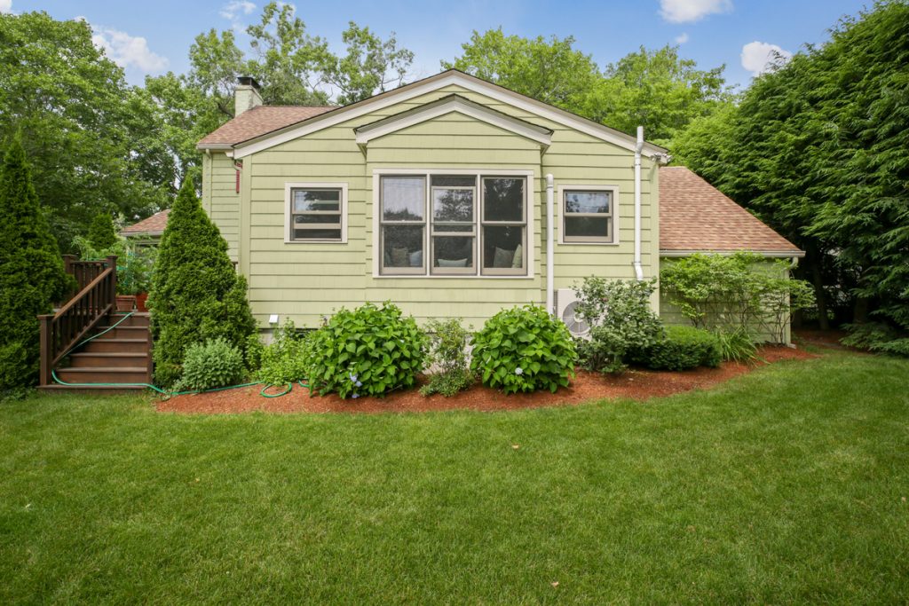 exterior of home that has a heat pump and is surrounded by green trees