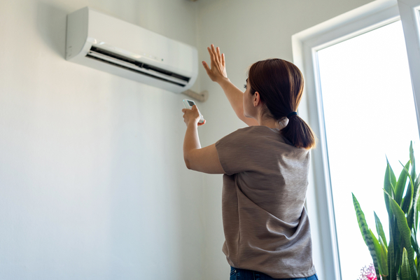Image of woman with her hand in front of a ductless mini split on wall circulating air into room